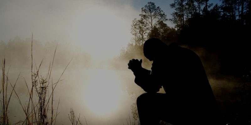 Genuflect.net image of man kneeling in prayer in front of pond at sunrise