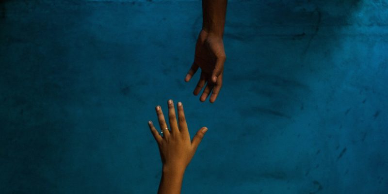 Two hands reaching for each other against a blue background