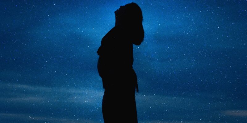 Silhouette of a pregnant woman at night looking up at the stars
