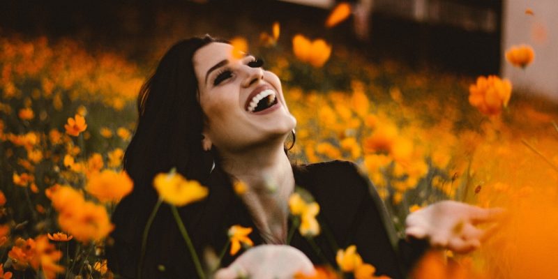 Woman outside in a field of orange flowers looking up to the sky and smiling with joy