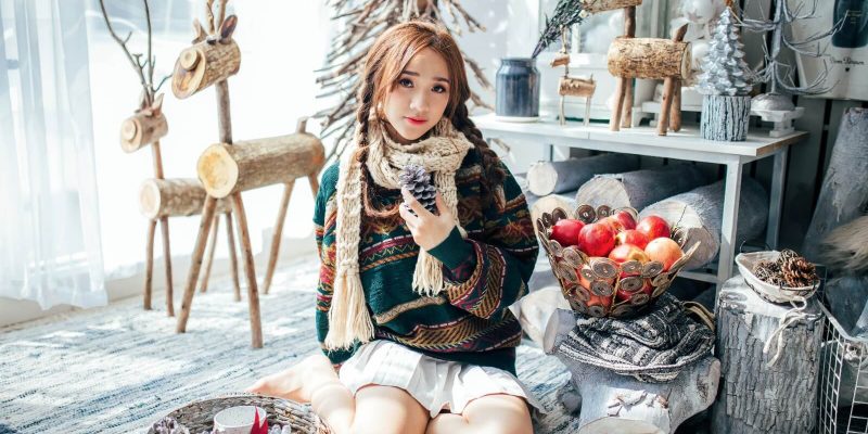 Girl in winter time with Christmas decor sitting on the floor holding a pine cone