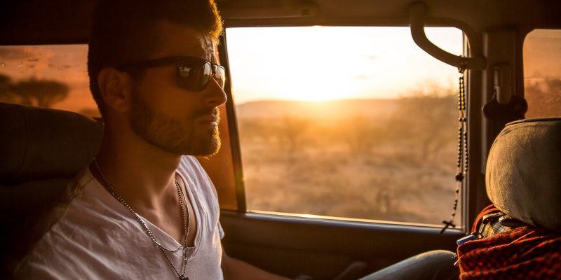 Guy wearing a t-shirt and dogtags riding in a car at sunrise