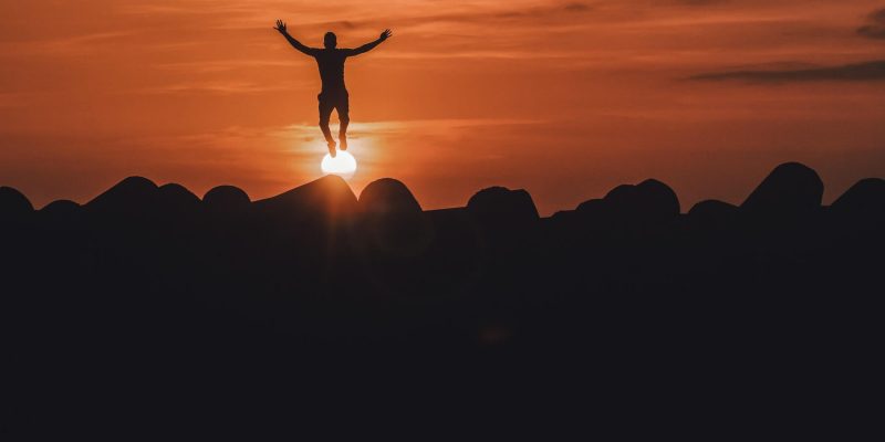 Silhouette of a man with arms outstretched to form a cross with the sun setting in the background