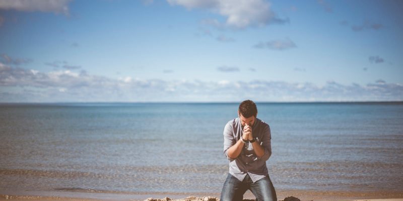 Man on his knees on the beach praying