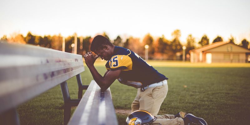 Football player kneeling at bench on the sidelines in prayer