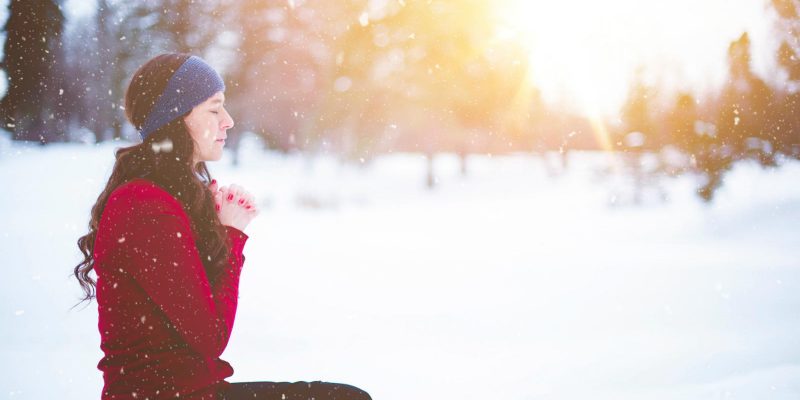 woman sitting in the snow with hands folded in prayer