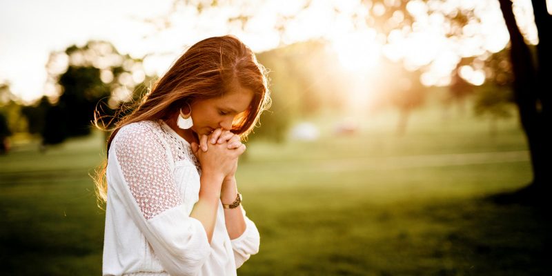 Woman with head bent down and hands folded in prayer
