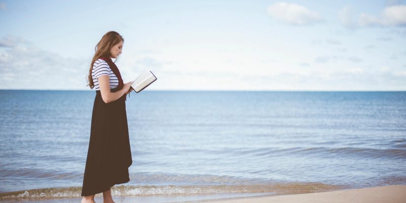Genuflect woman reading the bible on the beach