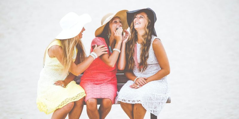 Three women sitting outside in the bright sun smiling and sharing secrets