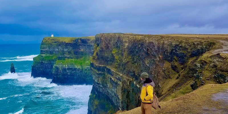 Man standing on the edge of the Cliffs of Moher looking out over the water