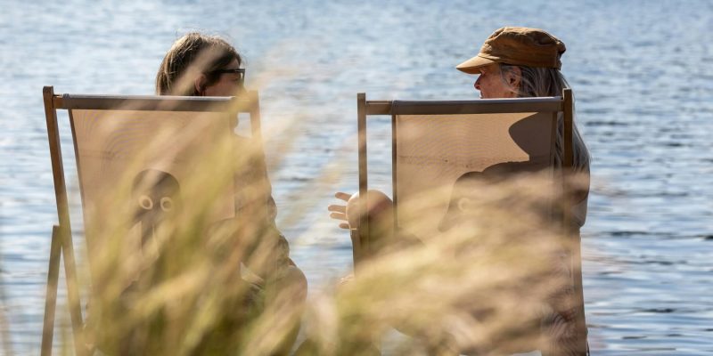 Two people sitting on the shore of a lake talking