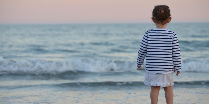 Young girl standing at the edge of the ocean at dusk looking out to sea