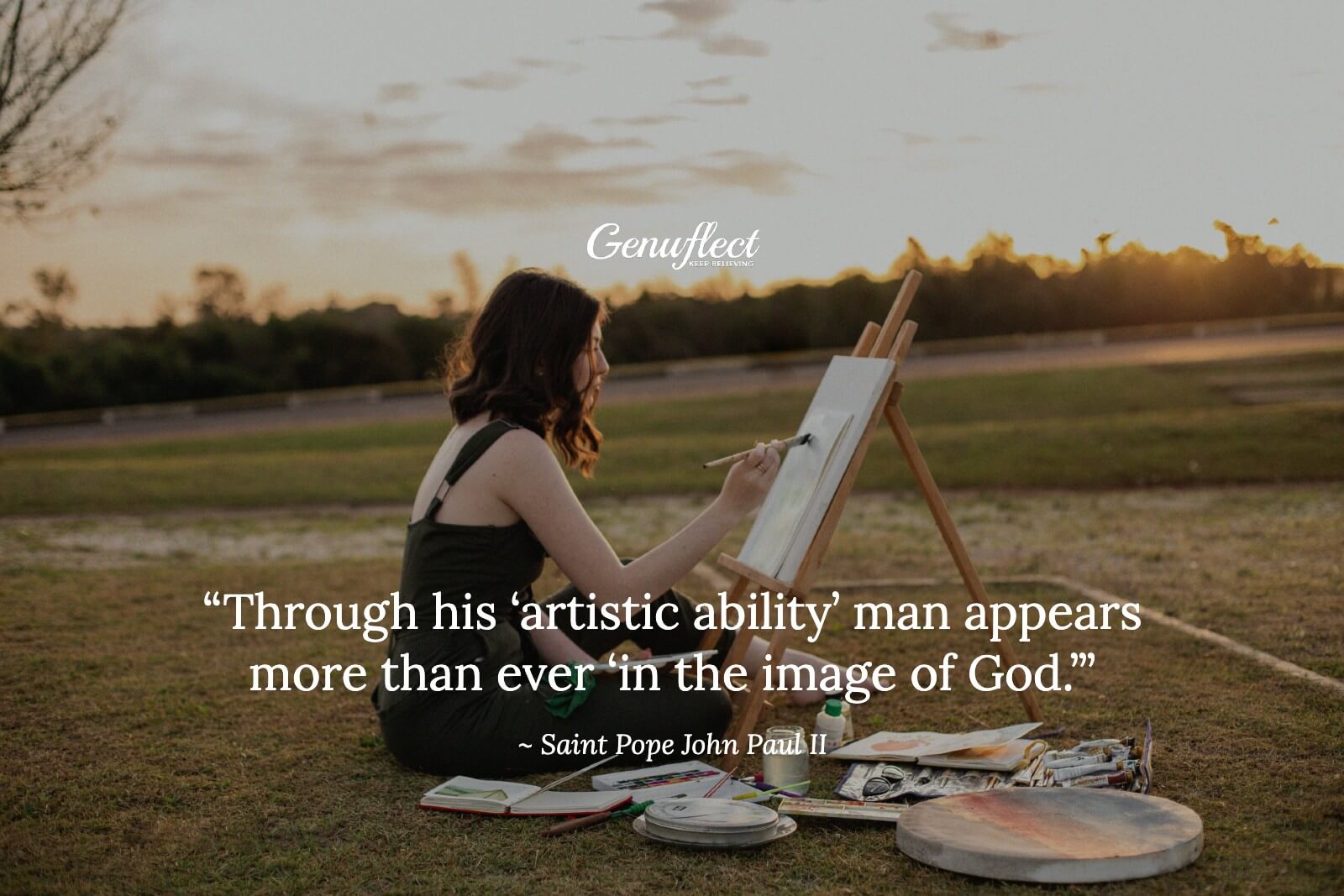 A woman sitting outside on the ground painting on a canvas on an easel.