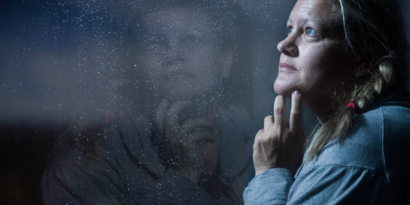 Woman staring out rainy window with reflection