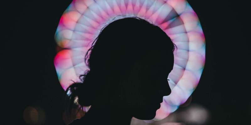 Silhouette of a woman's profile with her head bowed and a stained glass window in the background