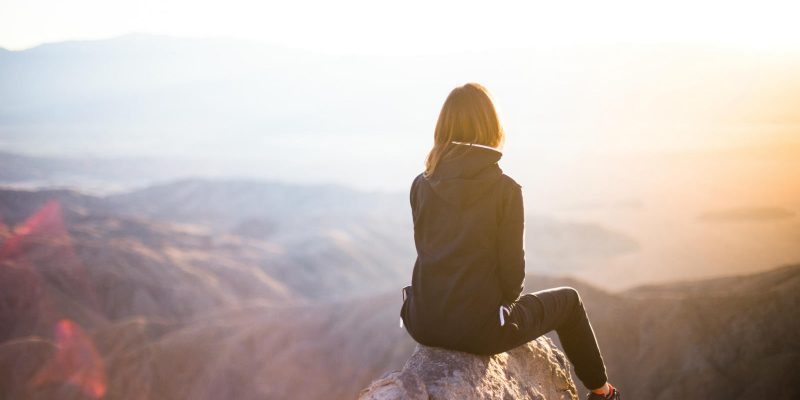 Woman sitting on top of a mountain looking out over the land at sunrise