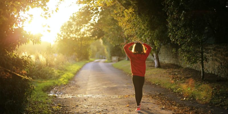 Woman walking alone on a country road at sunrise with her hands on top of her head