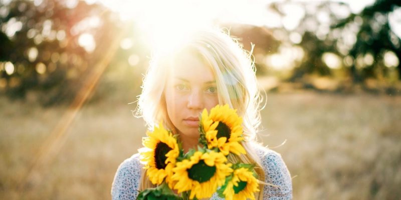 Girl holding a bunch of sunflowers with sun shining on her blonde hair from behind