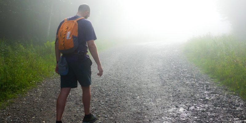 Man hiking with his head down on a dirt path on a foggy day and you can't see where the path leads