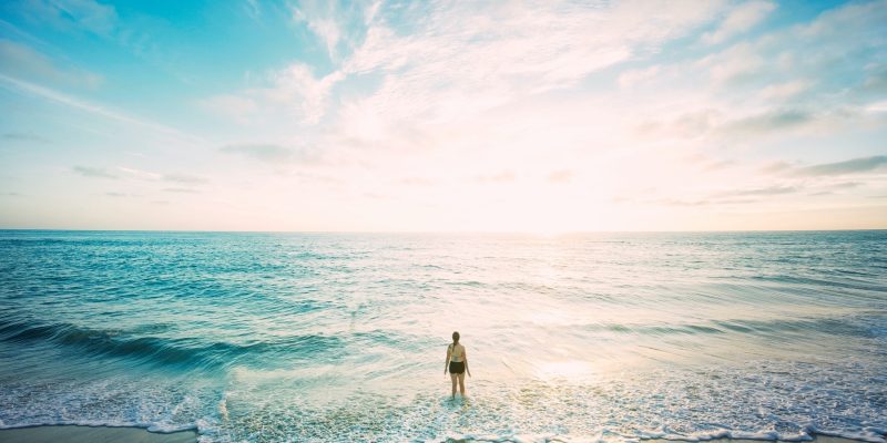 Woman standing on the beach water's edge watching sunrise