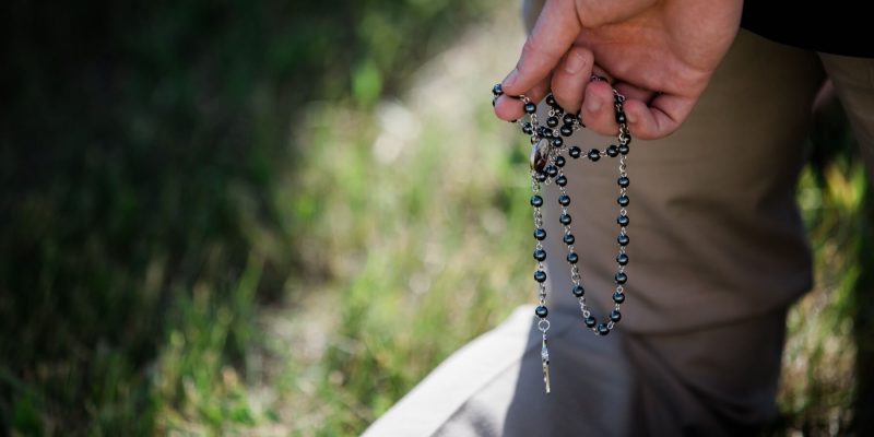 Close up of a man's hand holding a black rosary in prayer