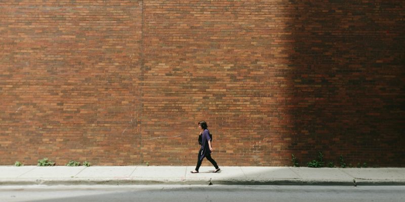 Person walking along the sidewalk next to a brick wall