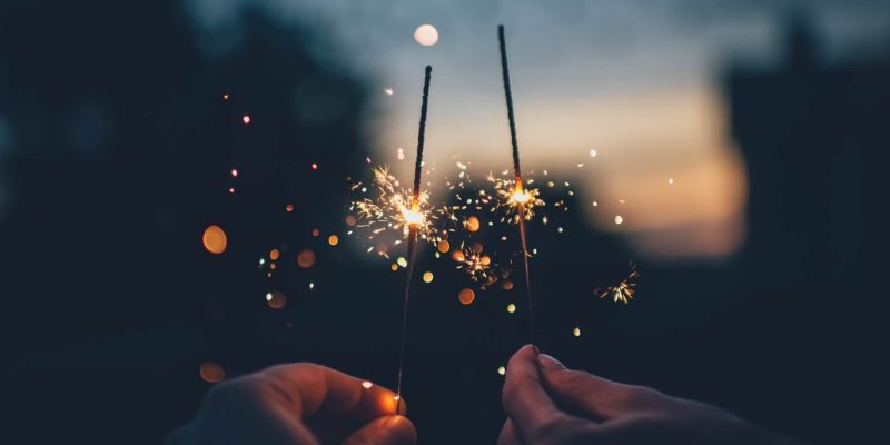 Close up of two hands holding lit sparklers