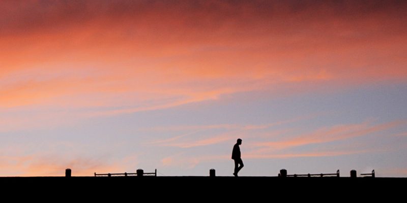 Silhouette of man walking against an orange sky at sunset