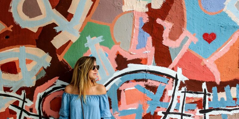 Woman standing against a wall painted with an abstract design of bright colors