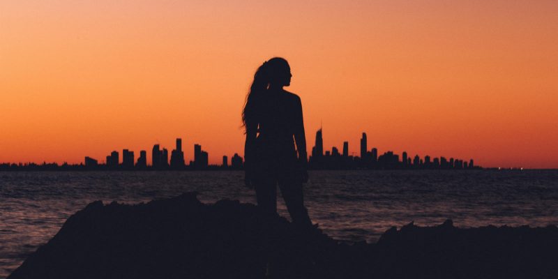 Woman standing on hill with city in the background at sunset
