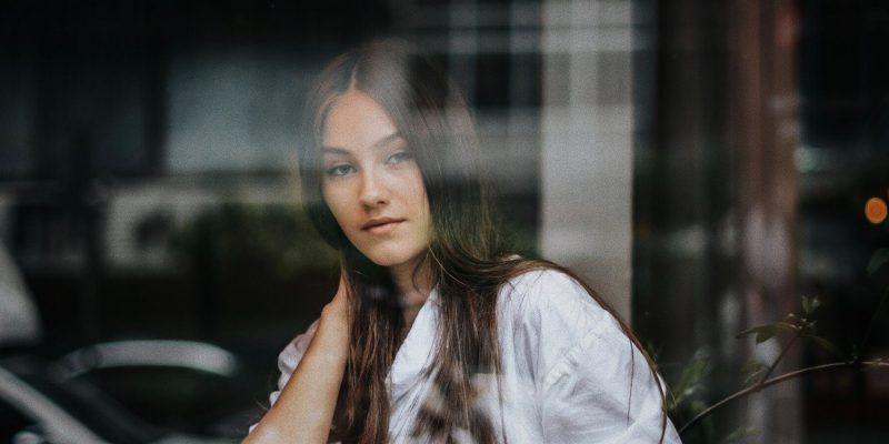 Girl sitting inside behind a window looking into the camera