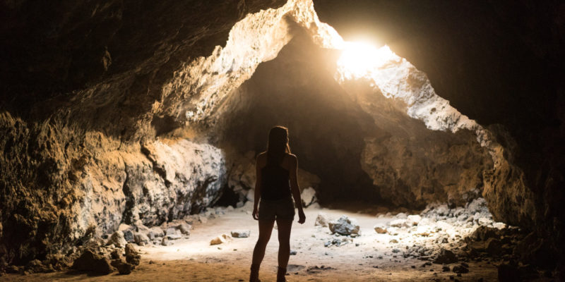 Woman in cave with bright light shining in from the top