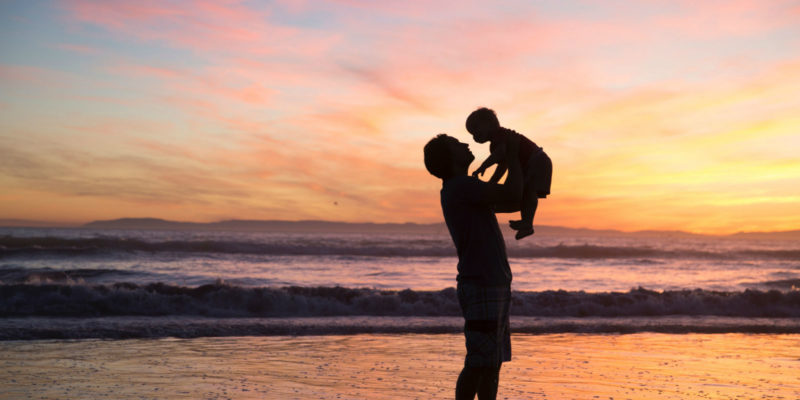 Dad holding child in the air at sunset on the beach