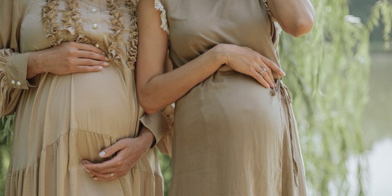 Two pregnant women side by side with hands on their pregnant bellies