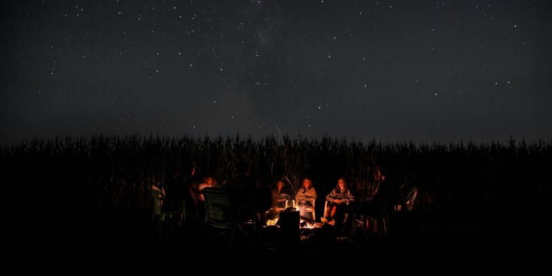 A group of people sitting around a campfire at night under a star-filled sky
