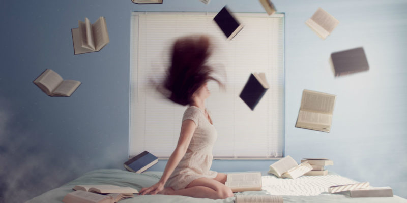 Woman sitting on her bed with books flying in the air