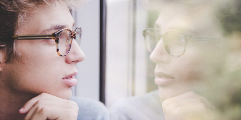 Close up of a guy looking out a window with his reflection in the window