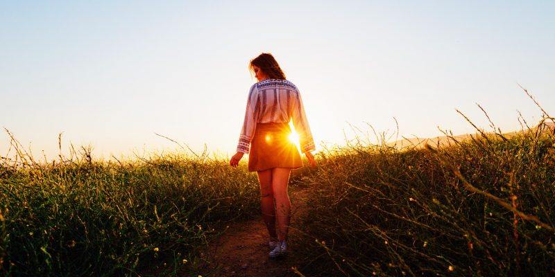 Woman walking up a path on a hill outside with sun coming up over the hill