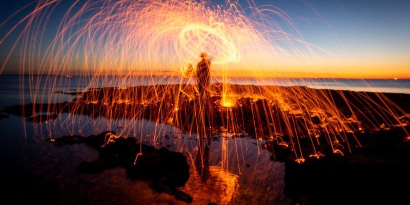 Person by the sea at dusk creating sparks