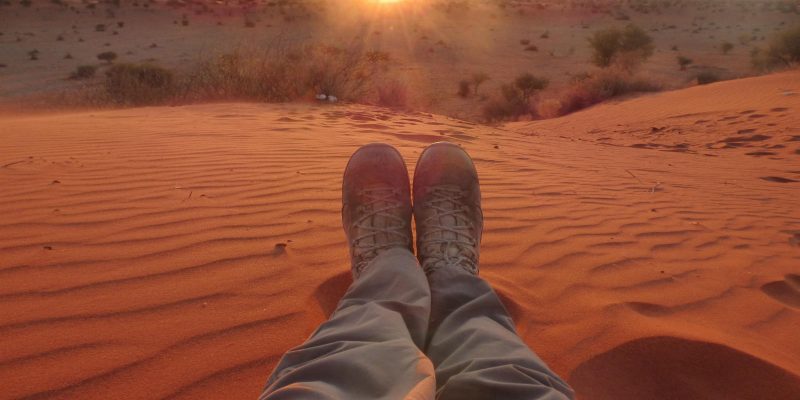 Man's outstretched legs sitting in the desert at sunrise