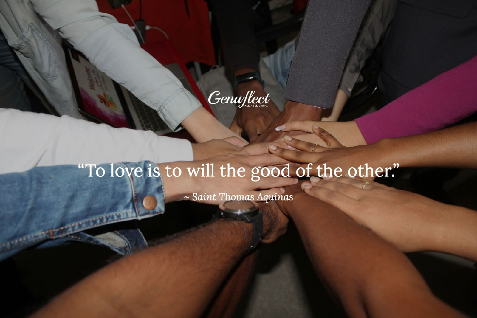 Multiple people standing in a circle with hands gathered in the center in unity