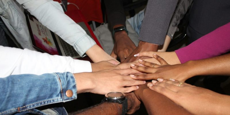 Multiple people standing in a circle with hands gathered in the center in unity