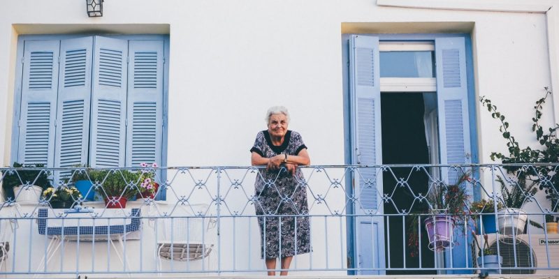 Elderly woman standing outside on her balcony leaning on the railing and smiling