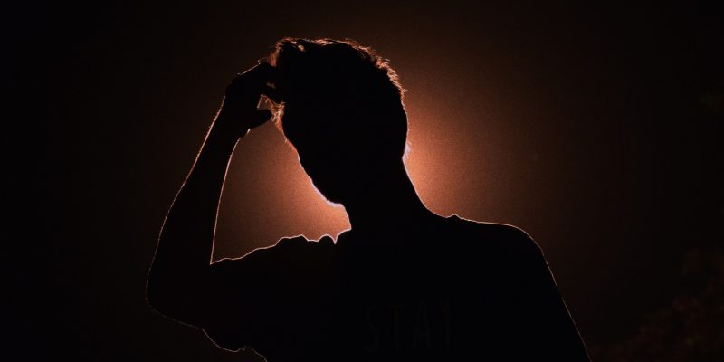 Silhouette of a man with his hand up to his forehead and light shinning behind him