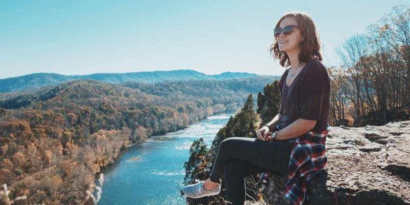 Woman sitting on a rock on a mountain top high above a river smiling and enjoying the sunshine
