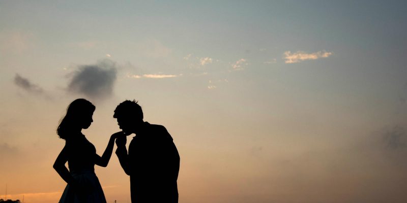 Silhouette of man kissing woman's hand at sunset