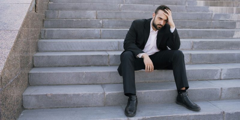 Man sitting on steps outside with his hand on his head in despair