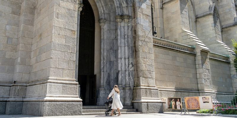 Woman walking with a baby carriage towards the open doors of St. Patrick's Cathedral in New York, NY